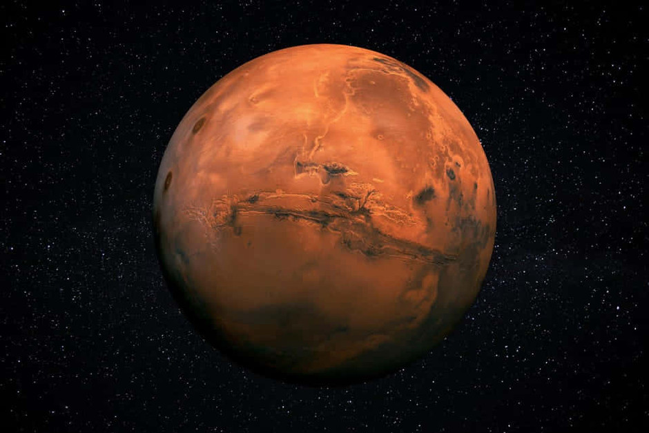 Mars, med Vallis Marineris, den största kända kanjonen i solsystemet, i mitten av bilden. Planeten är brunröd mot svart bakgrund. 