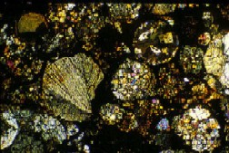 Bilden, tagen i ett polarisationsmikroskop, visar en kondrit som föll i Hallingeberg i Småland 1944. Bergarter av detta utseende existerar inte på jorden. Bilden ser ut som ett gytter av kristaller i olika färger.