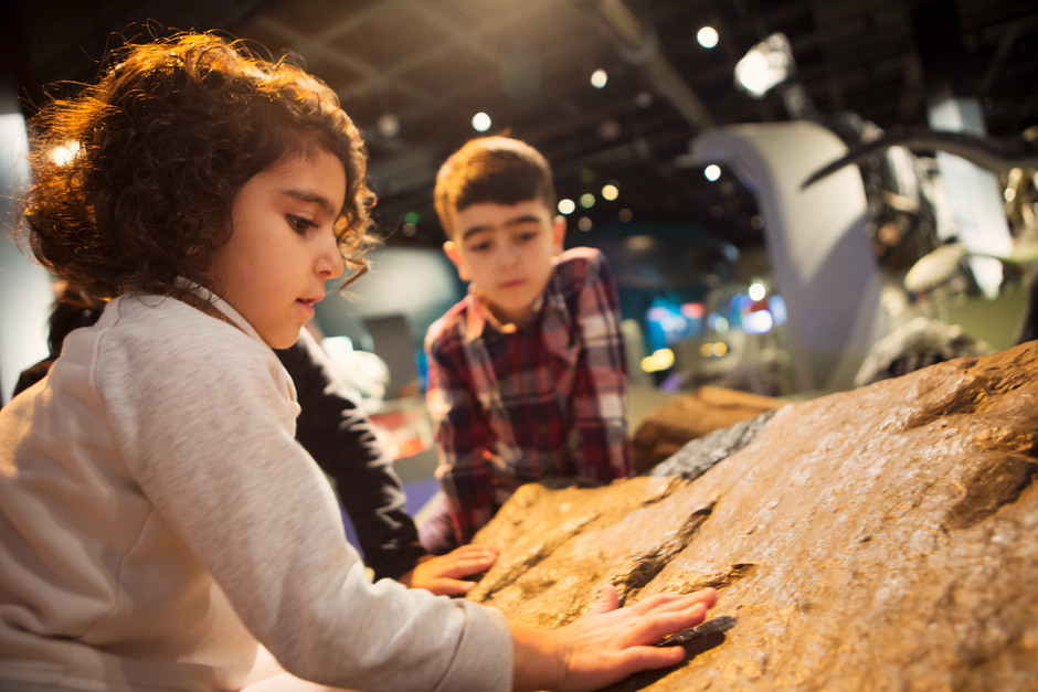 foto av ett barn som känner med handen på ett stenblock i utställningsmiljö. 