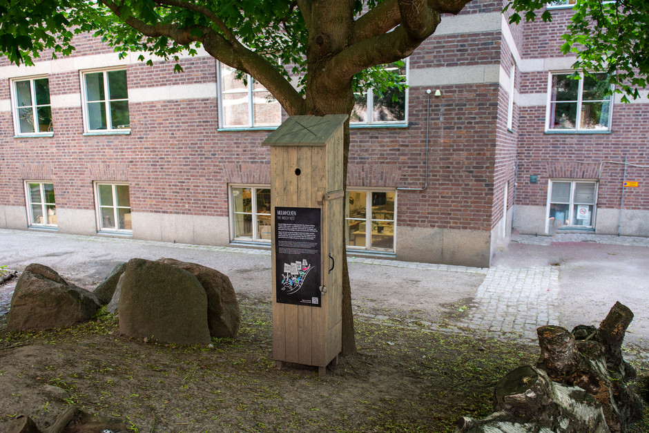 Hög träholk placerad mot ett träd med en skylt på framsidan, med texten mulmholk.
