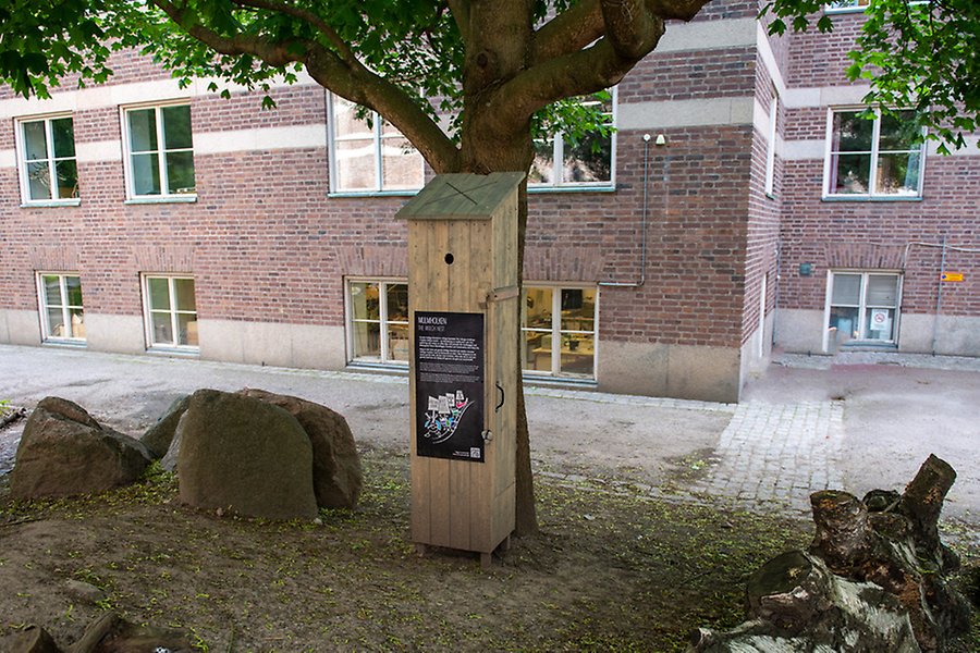 Hög träholk placerad mot ett träd med en skylt på framsidan, med texten mulmholk.
